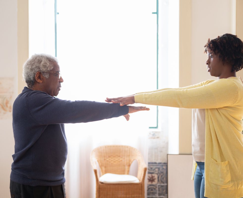 A caregiver guiding an older man through gentle stretching exercises at home